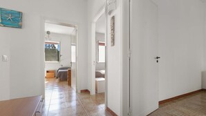 A hallway with a wooden bench, a white door, and a view into a bedroom with a bed and a window. - 2718 Villetta Soffio di Mare by Barbarhouse (Melendugno)