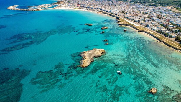 An aerial view of a coastal town with a clear blue sea, a sandy beach, and a rocky outcrop with boats. - 2718 Villetta Soffio di Mare by Barbarhouse (Melendugno)