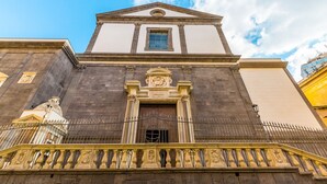 Une façade de style classique, avec une entrée centrale, flanquée de balustrades richement décorées et surmontée d’un fronton ornemental.
