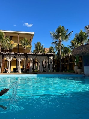 A swimming pool with a clear blue sky, palm trees, and a building with a tiled roof. - Wakanda Hotel (Andradina)