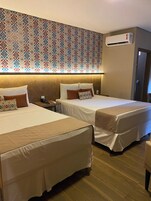 Habitación de hotel con dos camas, papel tapiz estampado, unidad de aire acondicionado y suelo de madera.
