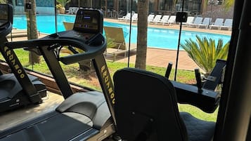 A gym with treadmills and exercise equipment, overlooking a pool and lounge area.