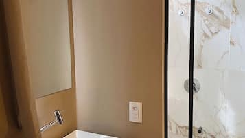 Un baño moderno con un lavamanos blanco, un espejo y una cabina de ducha de vidrio.