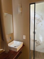 Un baño moderno con un lavamanos blanco, un espejo y una cabina de ducha de vidrio.