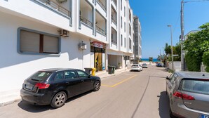 A street view with a black car parked on the left, a white building with a 'SUPERMERCATO' sign, and a clear blue sky. - 2993 La Casa di Tiziana by Barbarhouse (Melendugno)