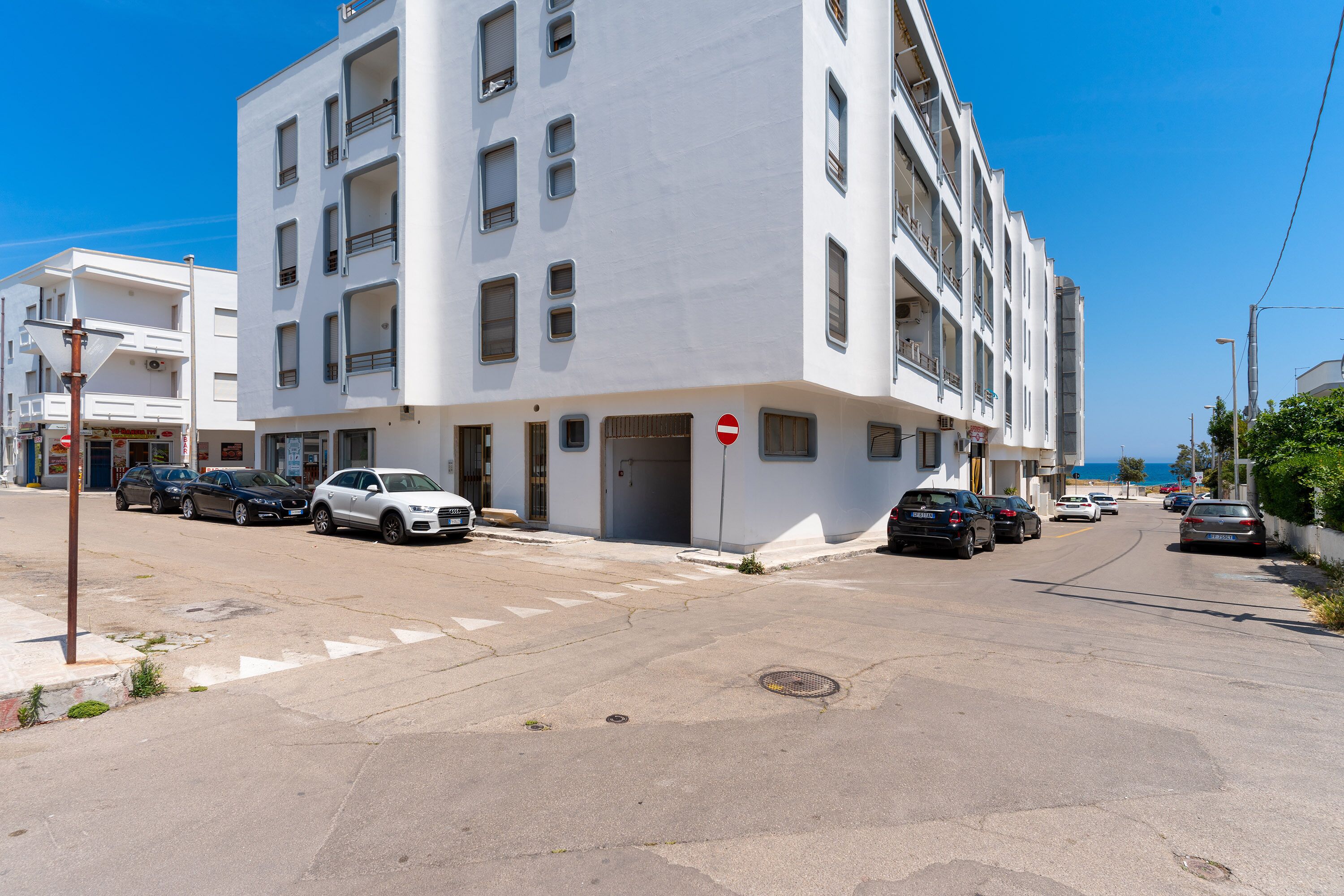 Ein mehrstöckiges Gebäude mit weißer Fassade, parkende Autos entlang der Straße und einem strahlend blauen Himmel.