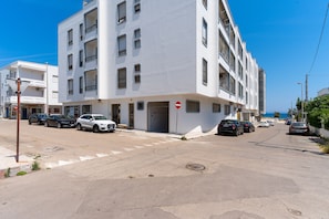 A multi-story building with a white facade, parked cars along the street, and a clear blue sky. - 2993 La Casa di Tiziana by Barbarhouse (Melendugno)