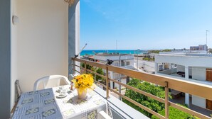 A balcony with a table set for two, a vase of yellow flowers, and a view of the sea and buildings. - 2993 La Casa di Tiziana by Barbarhouse (Melendugno)