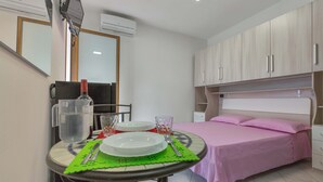 Ein Schlafzimmer mit einem Bett, einem Nachttisch mit rosafarbenem Bettwäsche, einem Spiegel und einem Fenster.