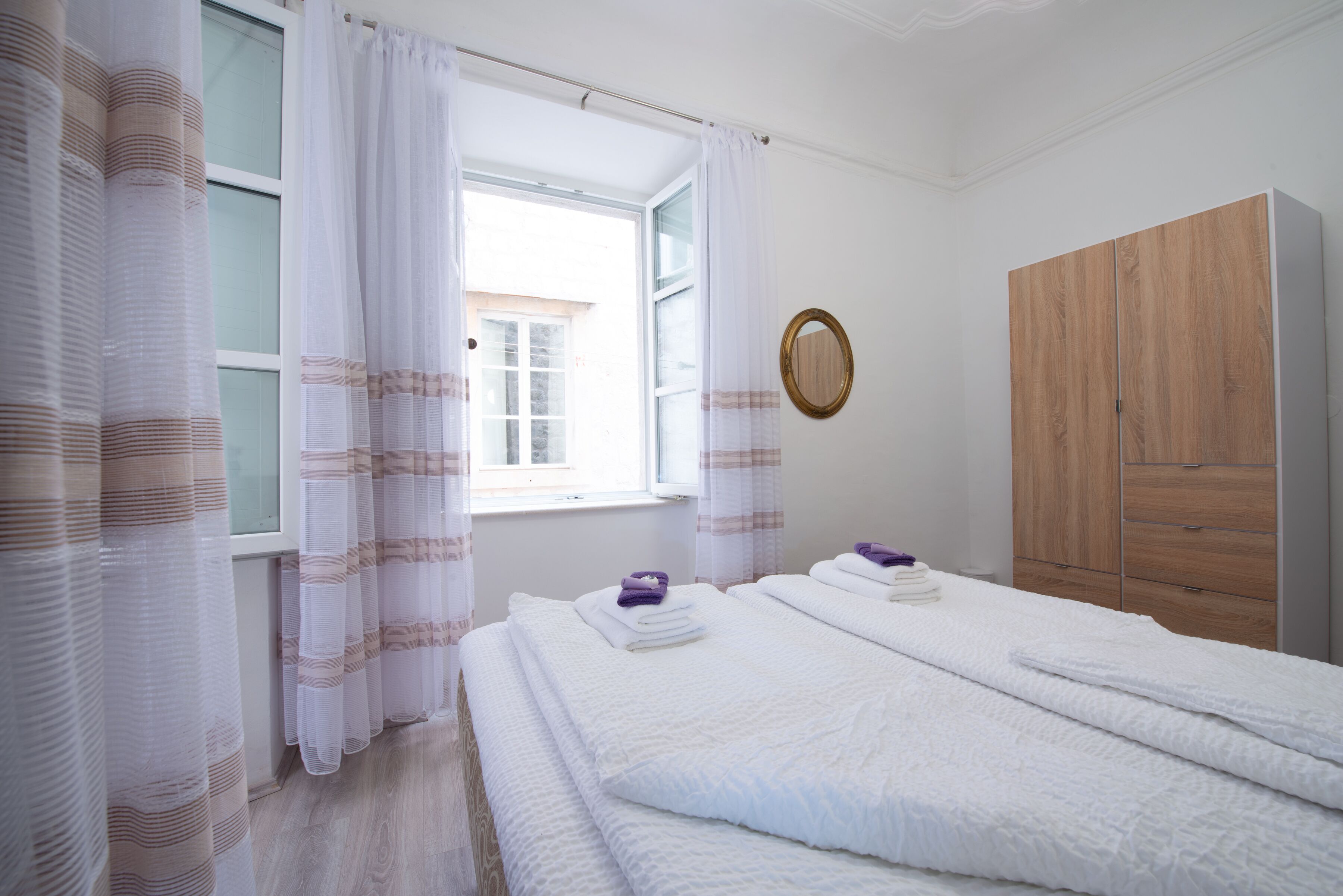 Une chambre à coucher avec un lit, une armoire en bois, une fenêtre avec des rideaux et un miroir au mur.