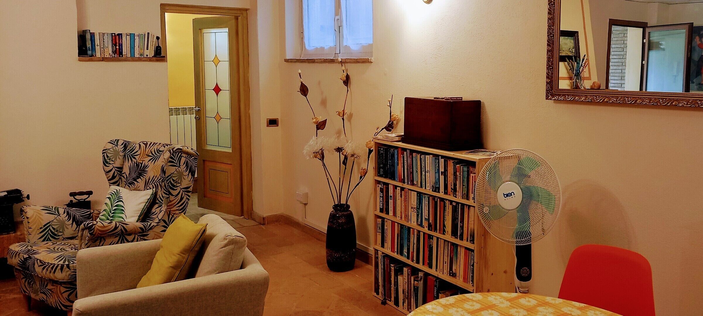 A cozy living room with a sofa, a bookshelf, a table, and a fan.