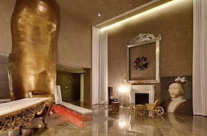 A luxurious lobby with a large golden sculpture, a fireplace, and a portrait.