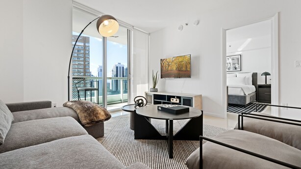 A modern living room with a sofa, a coffee table, and a view of the city through large windows. - ICON W BRICKELL EXCLUSIVE OCEAN VIEW 2BR/1BA #2909 (Miami)