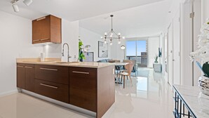 A modern kitchen with a large island, wooden cabinets, and a dining area with a glass table and chairs. - ICON W BRICKELL EXCLUSIVE OCEAN VIEW 2BR/1BA #2909 (Miami)