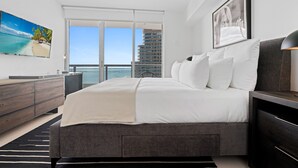A modern bedroom with a large bed, a dresser, a TV, and a balcony with a view of the city. - ICON W BRICKELL EXCLUSIVE OCEAN VIEW 2BR/1BA #2909 (Miami)