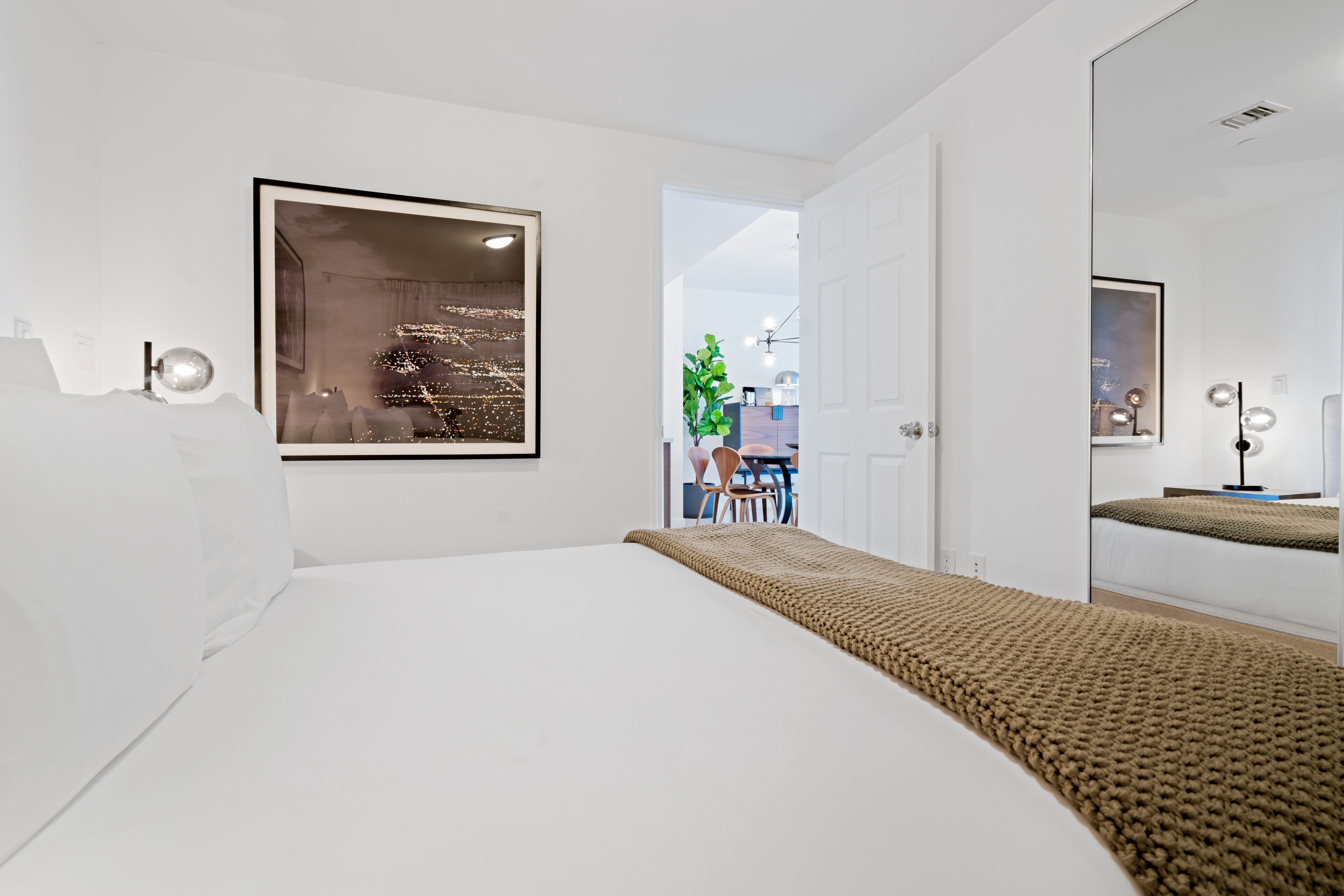 A modern bedroom with a large bed, a framed artwork on the wall, and a view of the outside.
