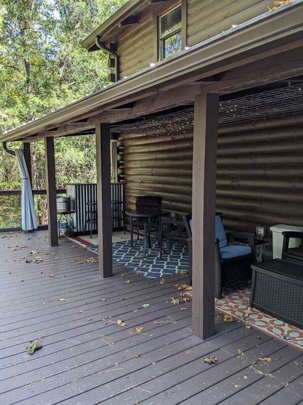 A covered outdoor deck with a rustic wooden cabin structure, a grill, and outdoor seating.