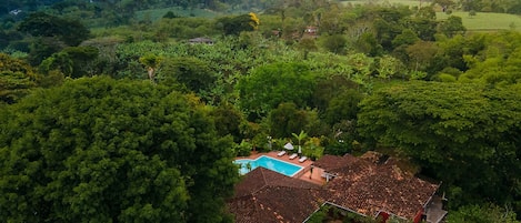 An aerial view of a house with a swimming pool surrounded by dense greenery.