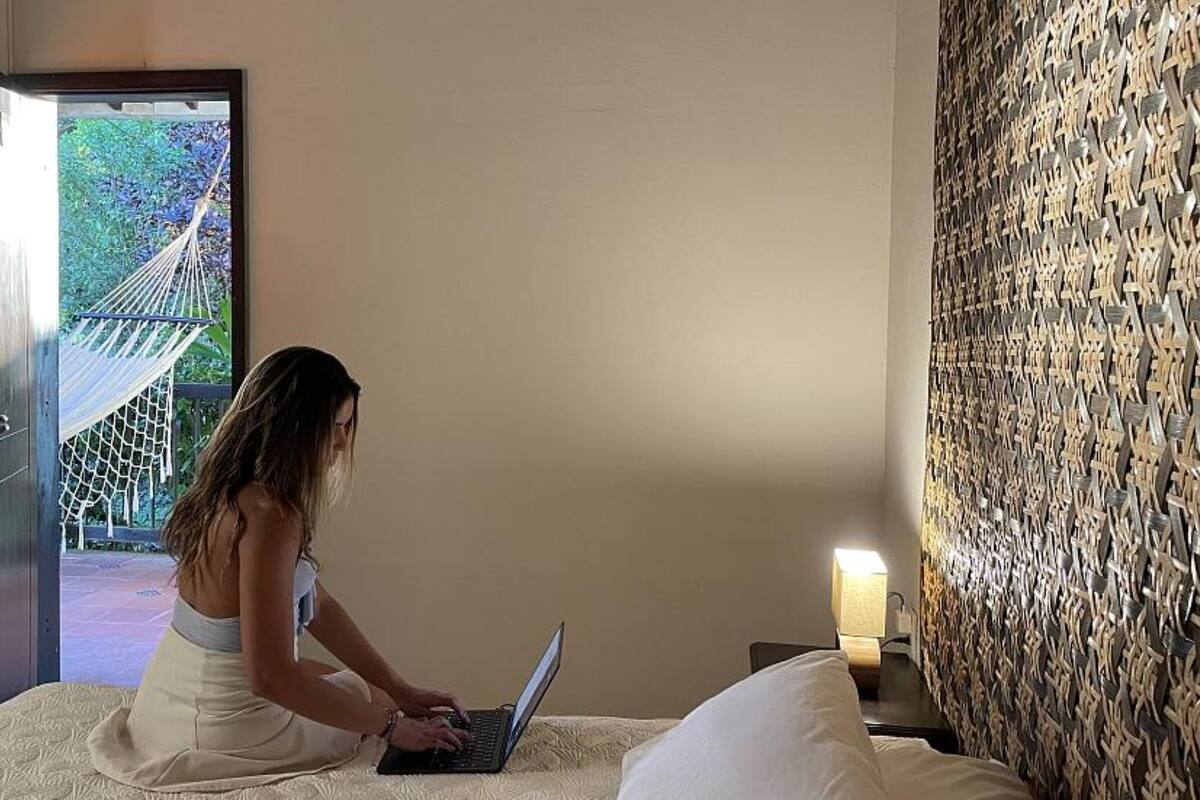 A room with a bed, a laptop, a door leading to an outdoor area, and a wall with a textured pattern.