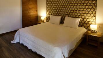 Una cama bien tendida con edredón blanco, dos mesitas de noche con lámparas y un cabecero estampado.