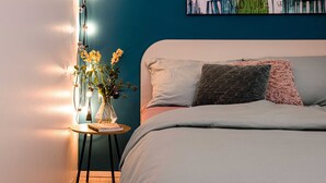 Un dormitorio con una cama, una mesita de noche con una lámpara y una pared decorada con un cuadro.