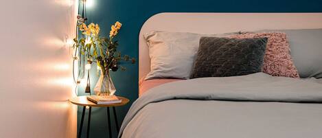 A bedroom with a bed, a bedside table with a lamp, and a wall with a painting.