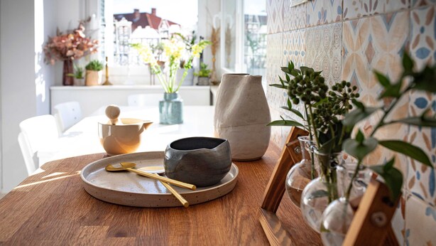 Una mesa de madera con un cuenco de cerámica, una cuchara y un florero con plantas.