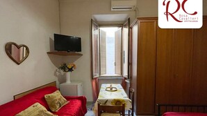 A cozy room with a red sofa, a small table with a vase of flowers, a television on a shelf, and a wooden wardrobe. - Cavalieri Affittacamere (Rome)