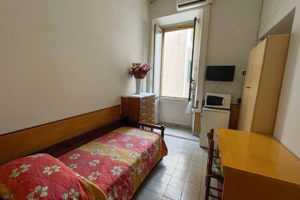 A bedroom with two beds, a dresser, a desk, a chair, a TV, and a window with an air conditioner.