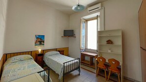 A small, well-lit bedroom with two beds, a desk, a chair, and a window with curtains. - Cavalieri Affittacamere (Rome)