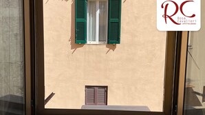 A window with green shutters, a view of a building with a beige facade, and a logo with "RC" and "Rosa Cavalieri". - Cavalieri Affittacamere (Rome)