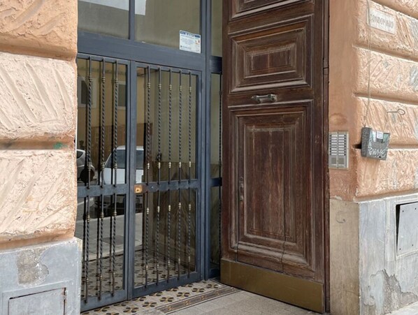 A wooden door with a metal gate, a stone wall, and a small mat at the entrance.