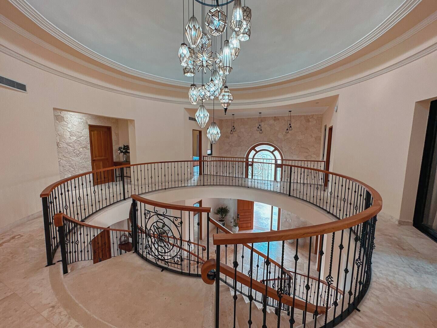A spacious, multi-level atrium with a central glass floor, a grand chandelier, and a curved railing.