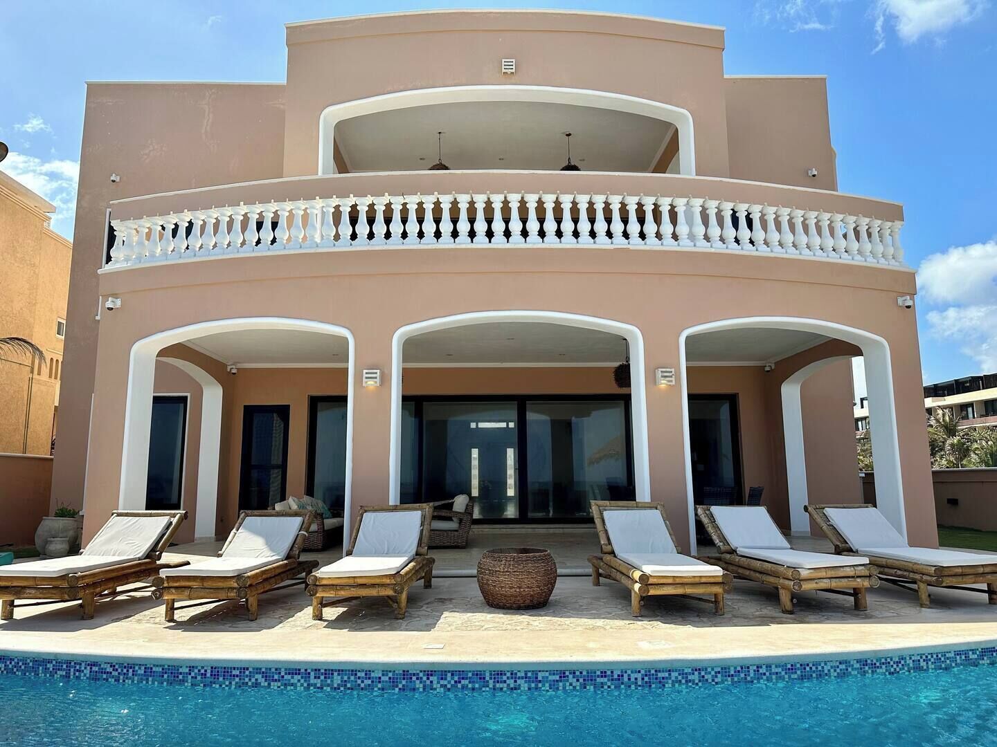 A two-story building with a pool, featuring a balcony with white balustrades and lounge chairs.
