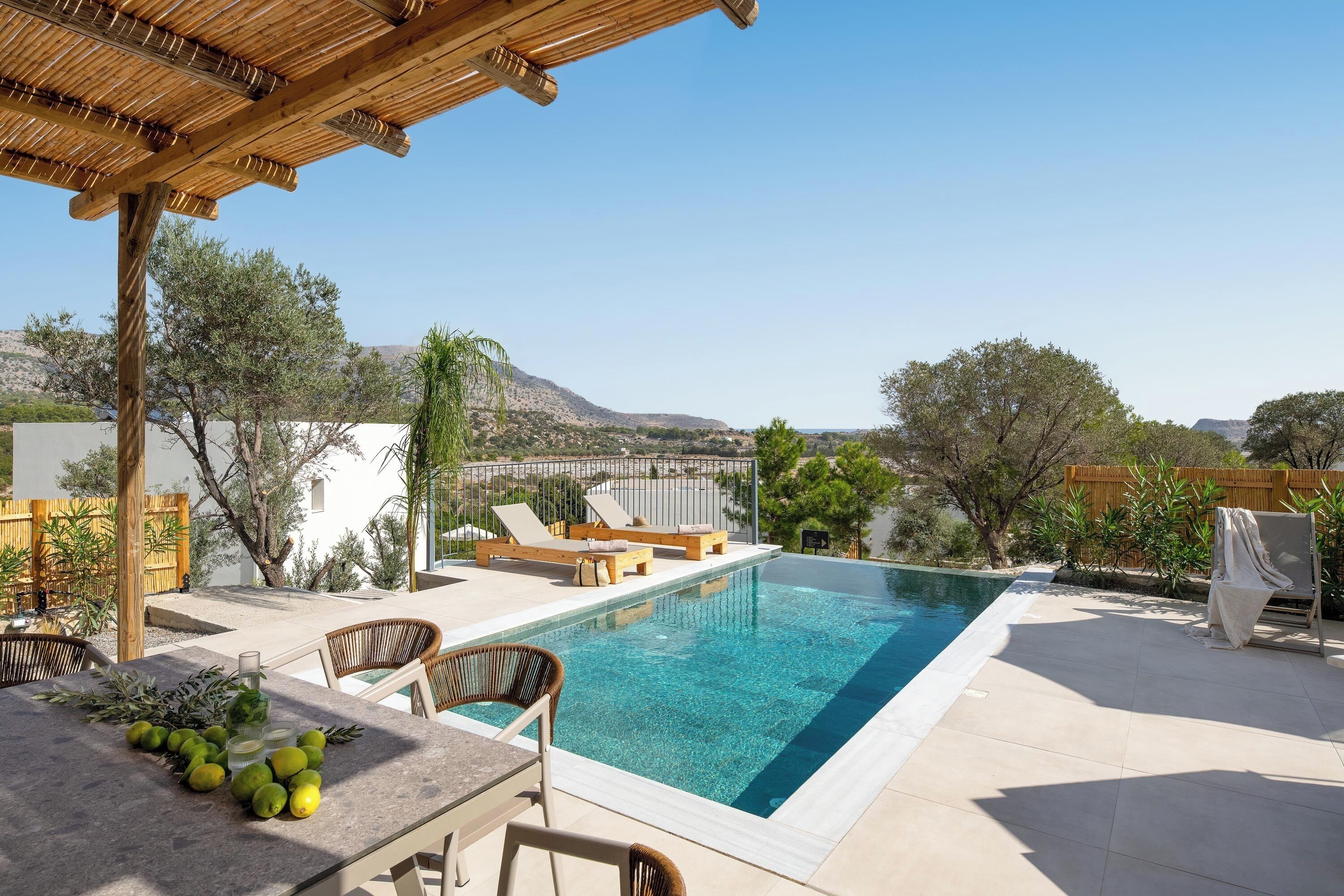 A poolside area with a pergola, lounge chairs, and a table with lemons and a bottle.