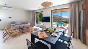 A modern living room with a dining table, sofa, and chairs, a TV, and a view of a pool.