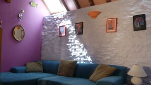Ein Wohnzimmer mit einem blauen Sofa, einem kleinen Tisch mit einer Lampe und einer Wand mit strukturierter Gestaltung und gerahmten Bildern.