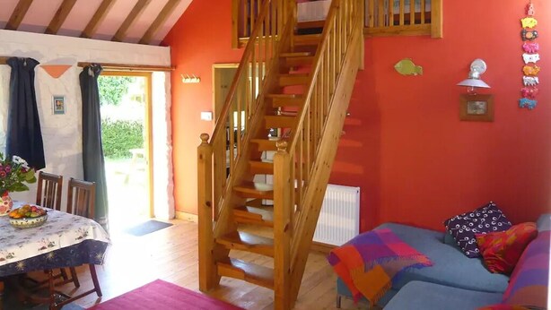 Ein Zimmer mit einer Holztreppe, einem Esstisch mit Stühlen, einer Couch und einer Heizung.