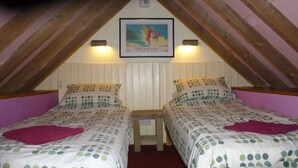 Ein Schlafzimmer mit zwei Betten, jedes mit einem Betttuch mit Punkten, einem gerahmten Poster darüber und einer Holzbalkendecke.