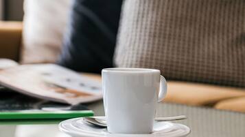 A white cup on a saucer on a table with a magazine and a pen beside it.