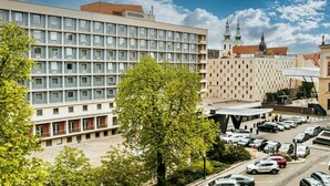 A modern hotel with a parking lot and a historic building in the background.