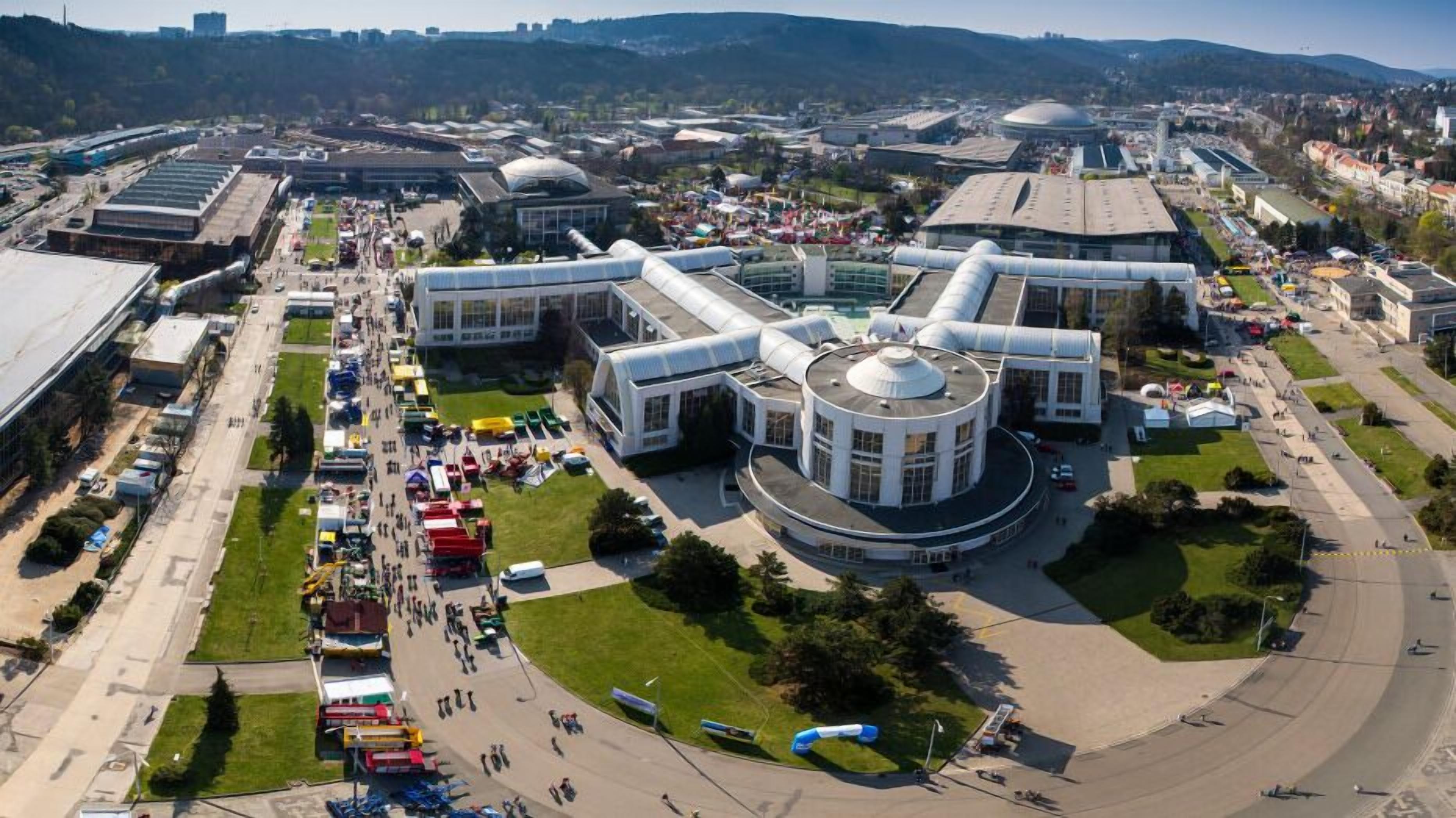 An aerial view of a modern building complex with a central circular structure, surrounded by open spaces and smaller buildings.
