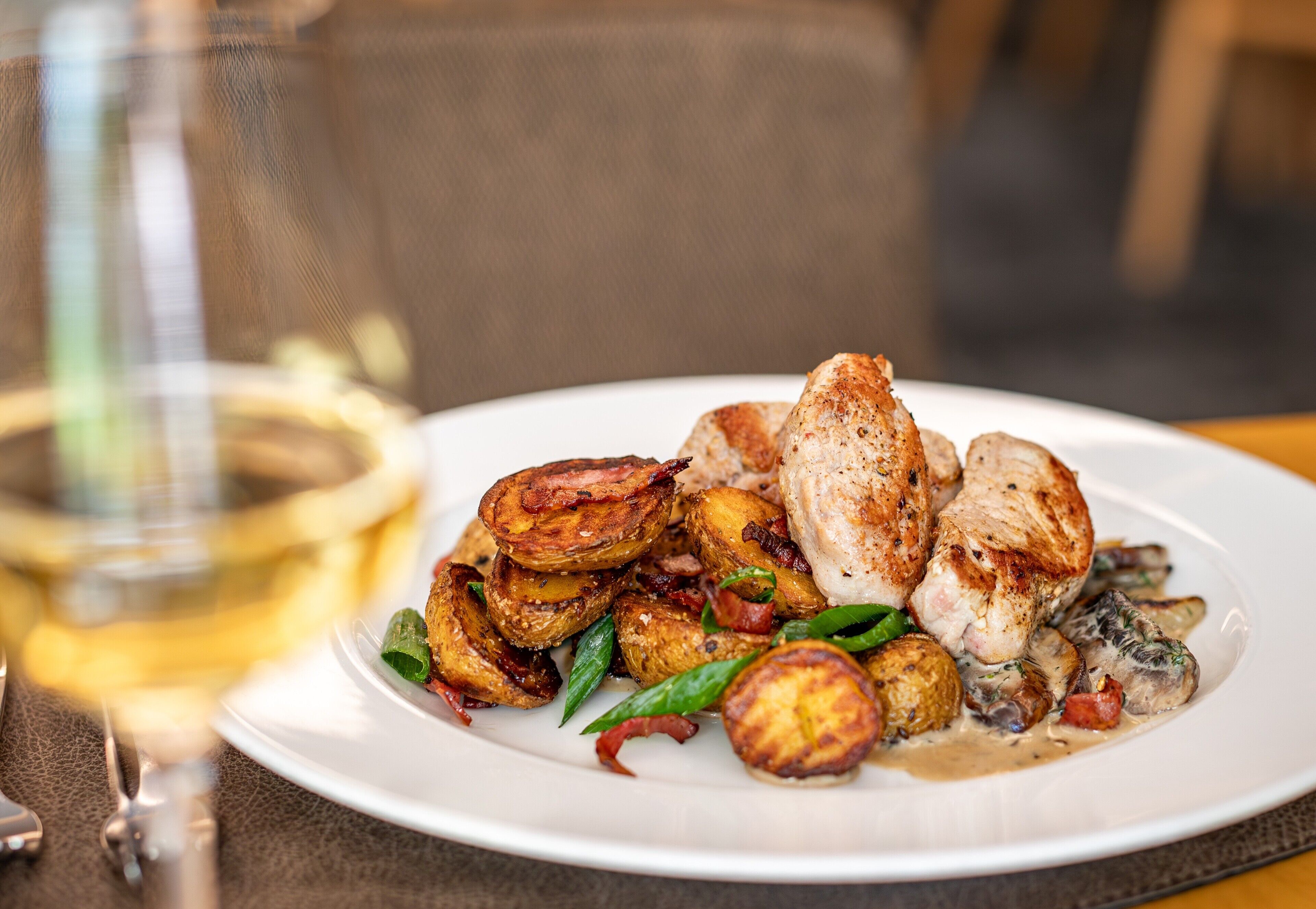 Une assiette de nourriture comprenant des pommes de terre rôties, du poulet et des champignons, accompagnée d'un verre de vin blanc.