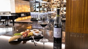 A wine bottle, a glass of wine, and a plate with food on a bar counter in a hotel lobby. - Hotel International Brno (Brno)