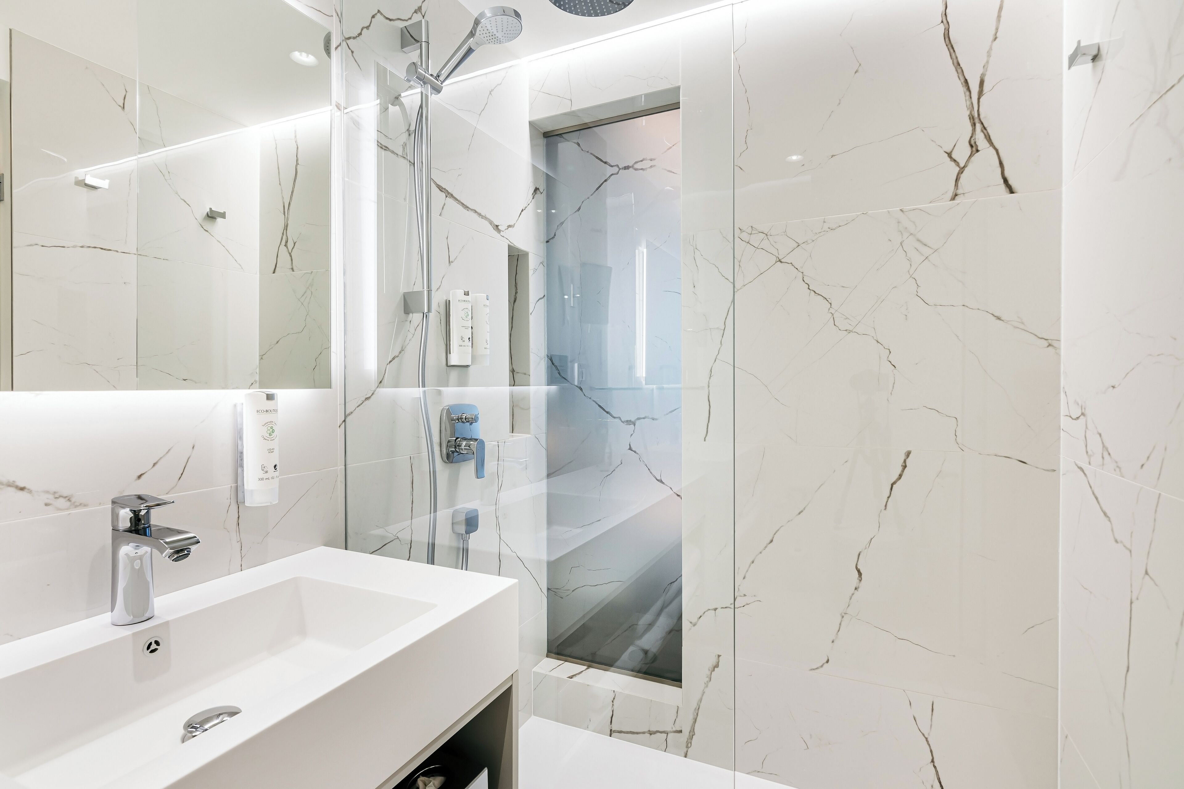 A modern bathroom with a white marble sink, a glass-enclosed shower, and a marble wall.