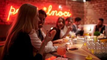 Eine Gruppe von Personen speist in einem Restaurant, im Hintergrund eine Ziegelwand und ein Neonzeichen.