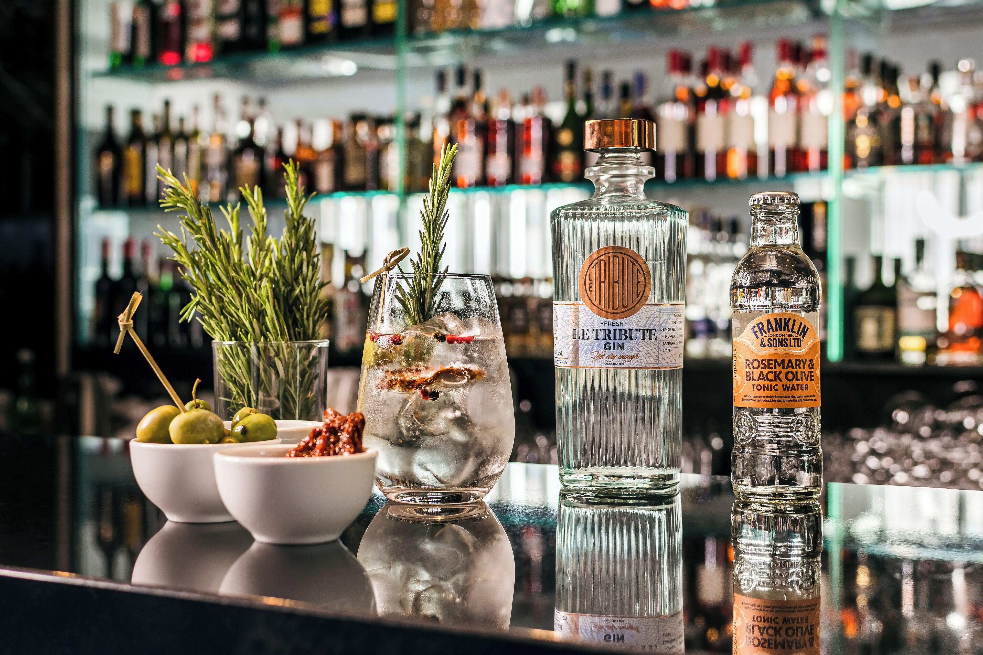 A bar counter with a variety of liquor bottles, a glass with a cocktail, and fresh herbs.