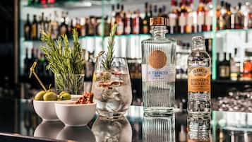 A bar counter with a variety of liquor bottles, a glass with a cocktail, and fresh herbs.