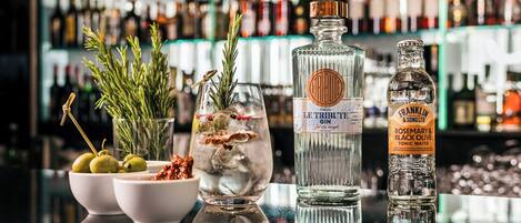 A bar counter with a variety of liquor bottles, a glass with a cocktail, and fresh herbs.