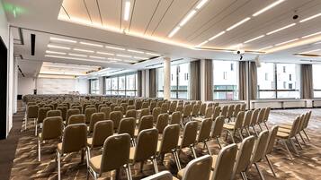Un amplio salón de conferencias con filas de sillas, piso alfombrado y un techo moderno con iluminación lineal.